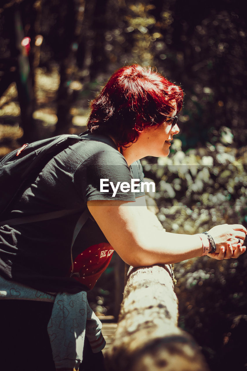 Side view of woman with redhead standing by railing in forest