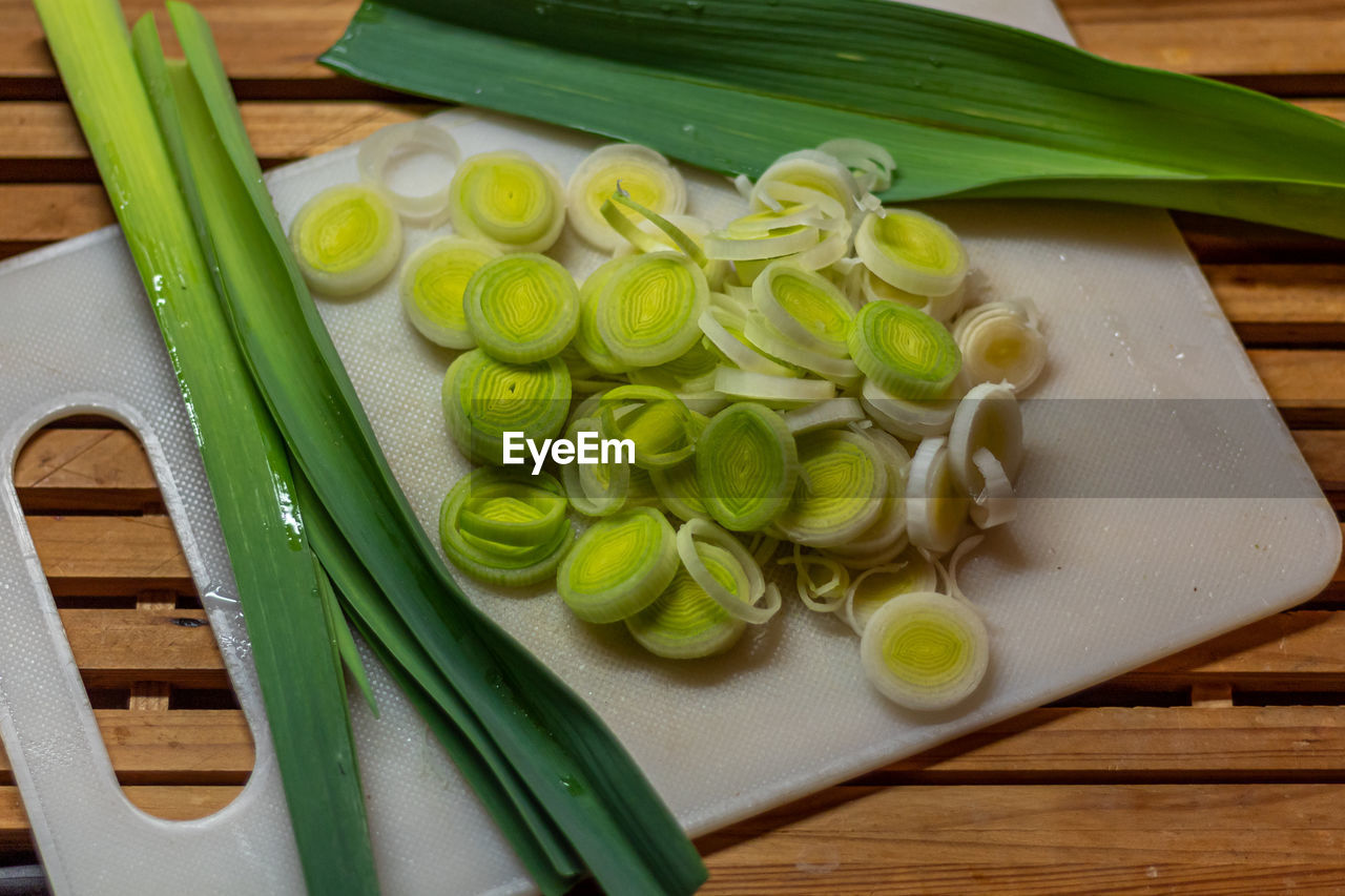 food and drink, food, freshness, healthy eating, leek, vegetable, wellbeing, cutting board, produce, plant, wood, indoors, dish, high angle view, green, kitchen knife, still life, no people, table, slice, fruit, ingredient, spice, raw food, spring onion, domestic room, kitchen, onion