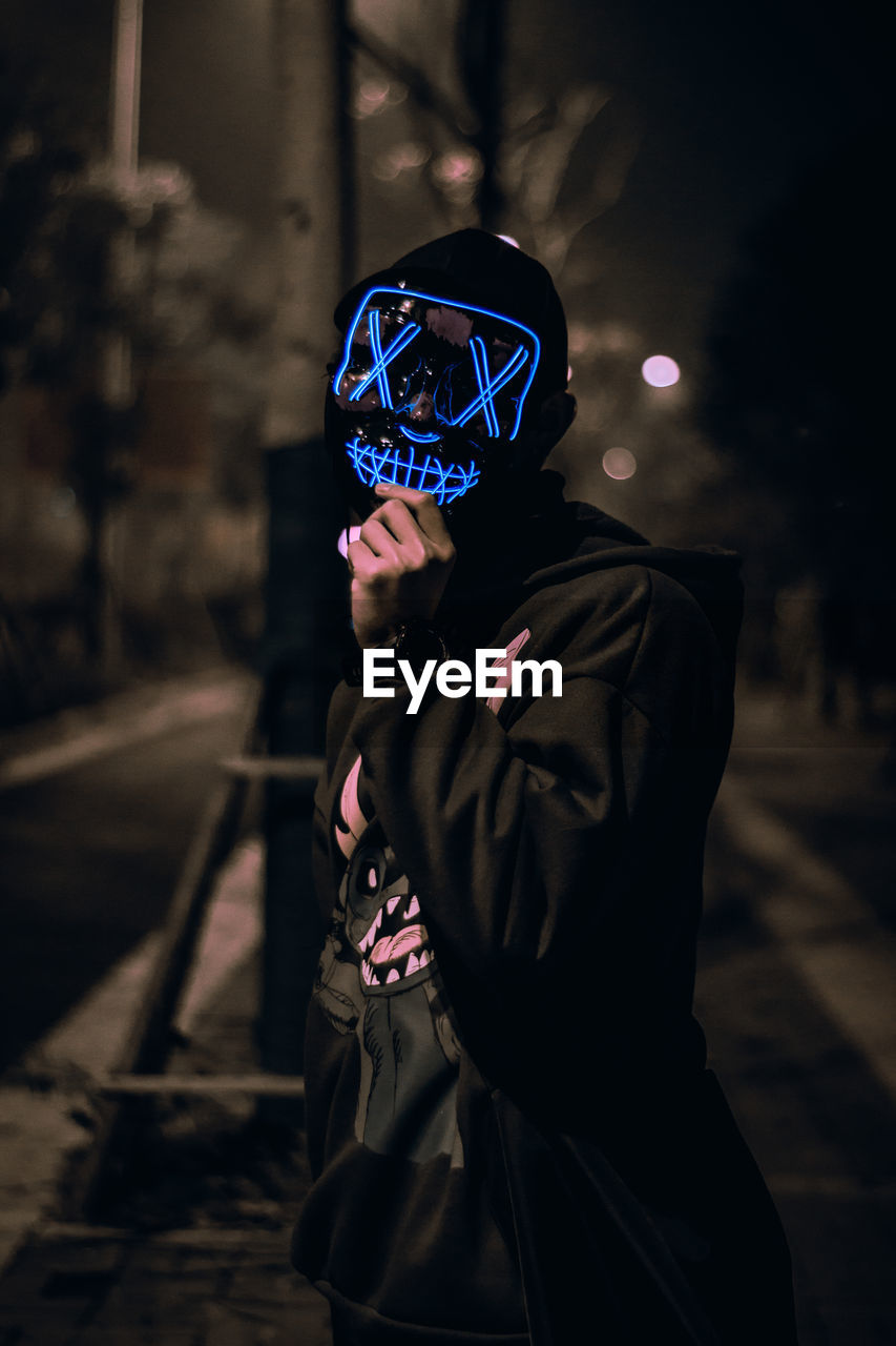 Portrait of the unknown man behind the neon mask on street at night. dark brown tone