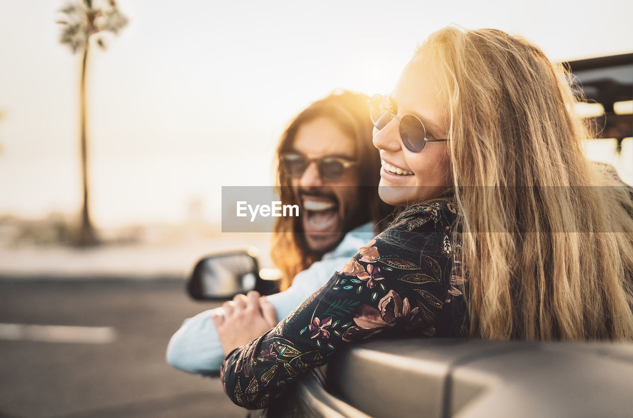 Cheerful couple wearing sunglasses traveling in convertible