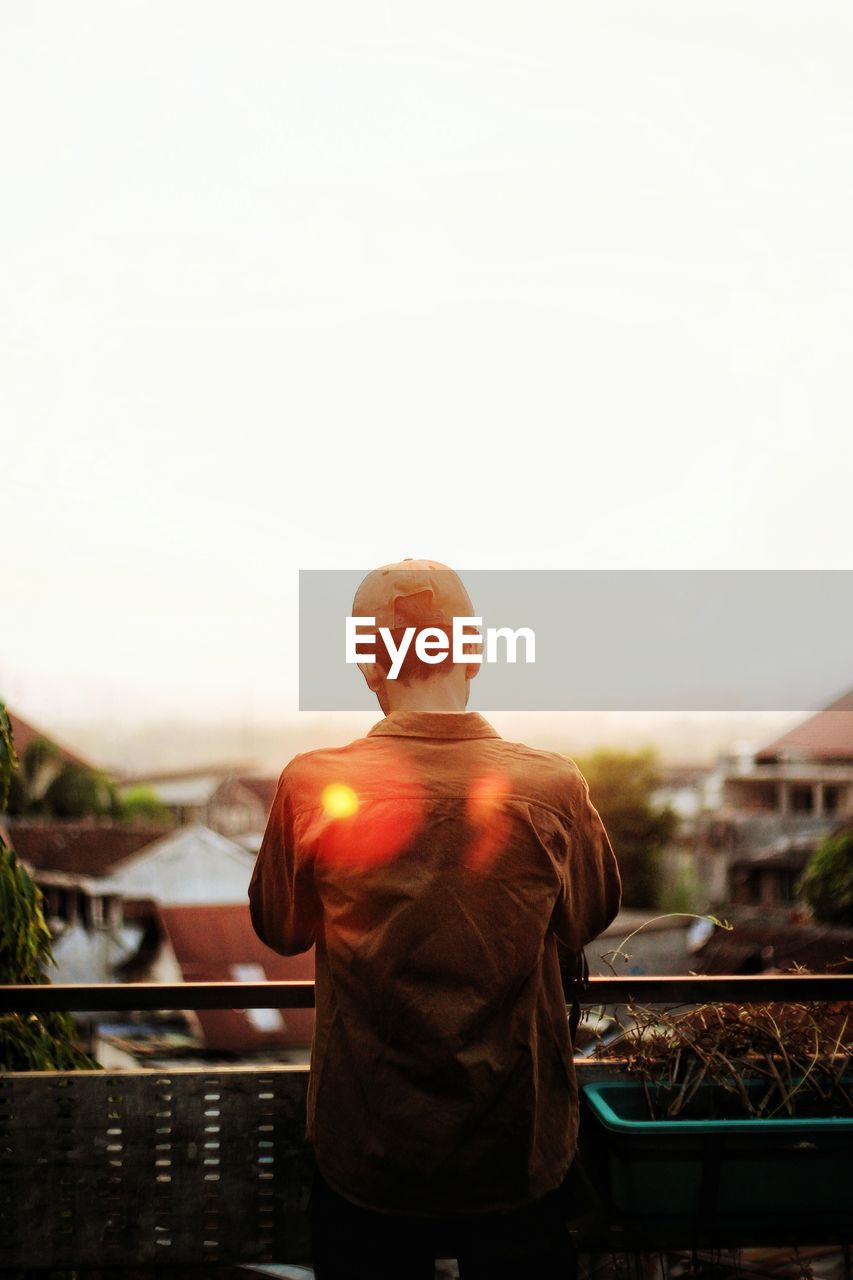 Rear view of man standing by railing against sky during sunset