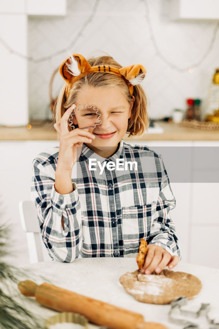 The girl is holding a cookie cutter in her hands, there is dough on the table. 