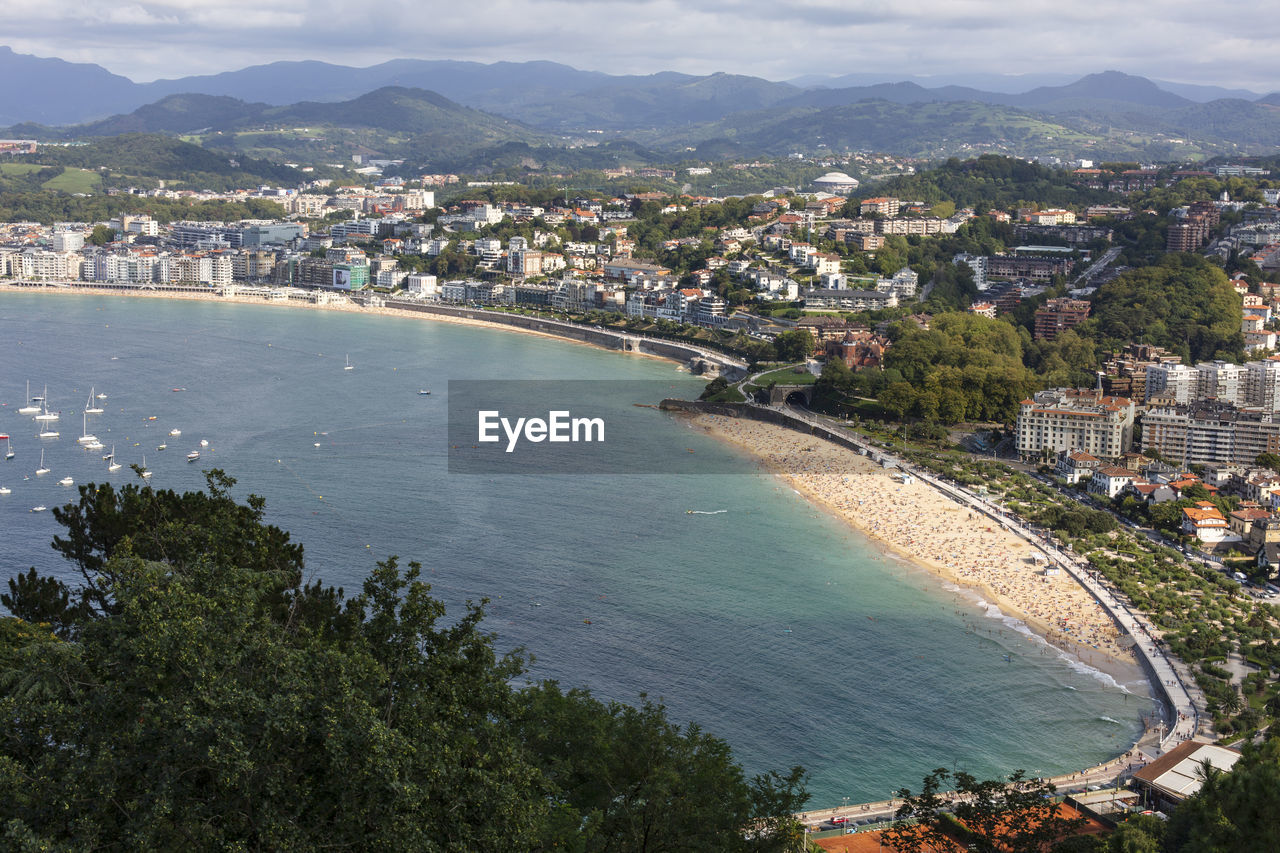 HIGH ANGLE VIEW OF CITY BY SEA AGAINST MOUNTAINS