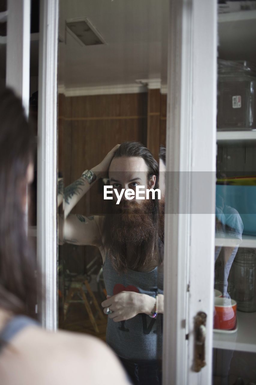 Reflection of bearded man standing at home