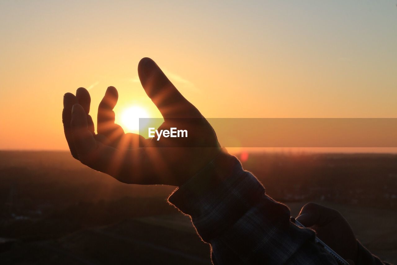 Close-up of silhouette hand against sun during sunset