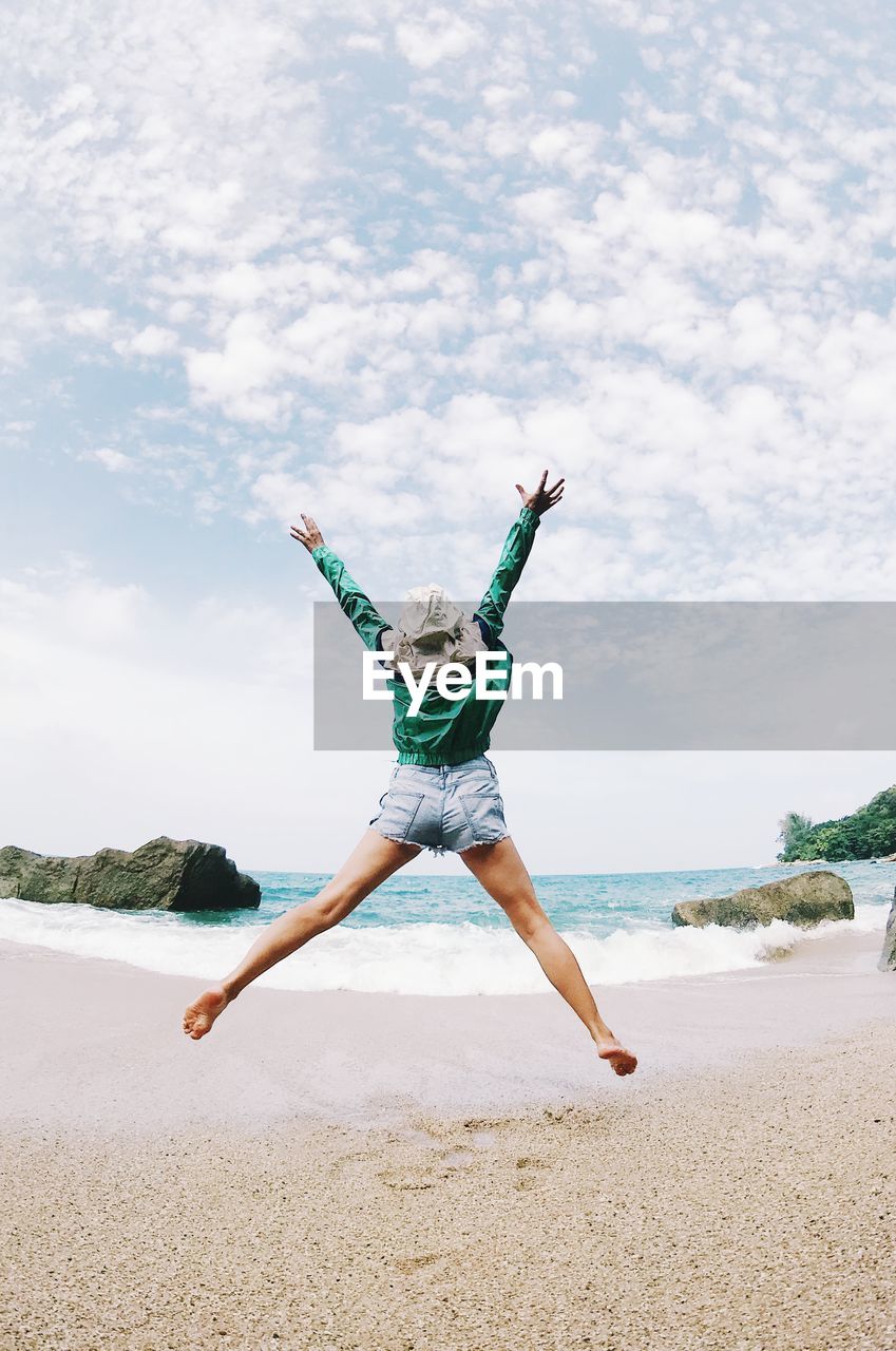 Rear view of woman with arms raised jumping against sea at beach