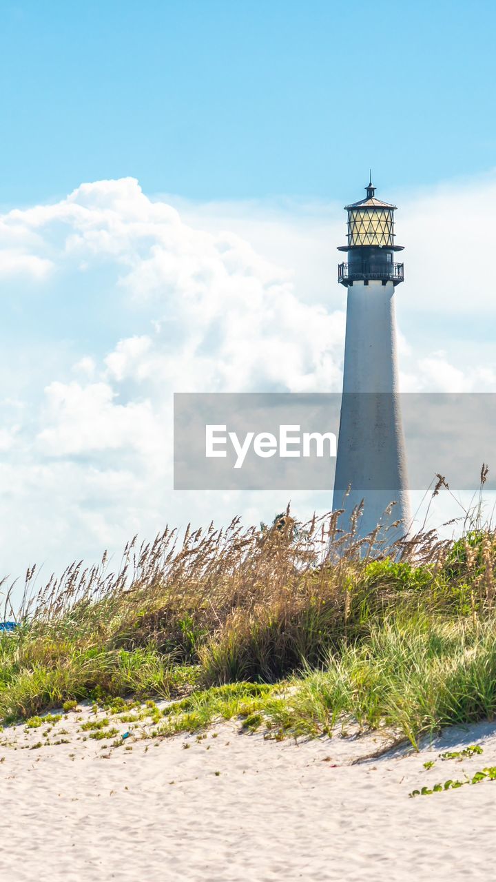 lighthouse by sea against cloudy sky