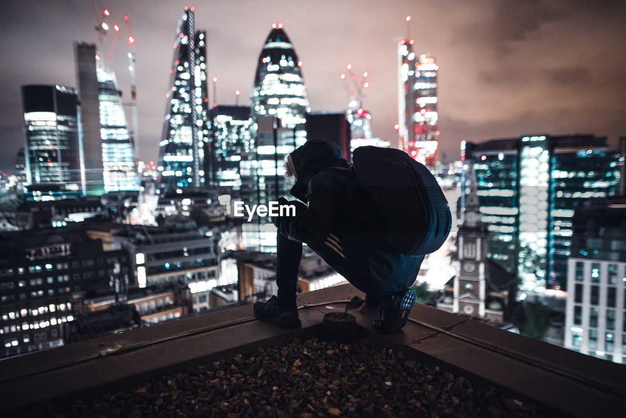 Rear view of man on illuminated cityscape against sky at night