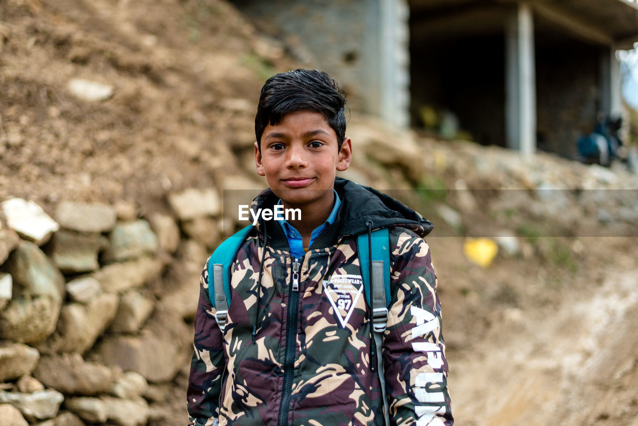 PORTRAIT OF SMILING BOY STANDING AGAINST STONE WALL