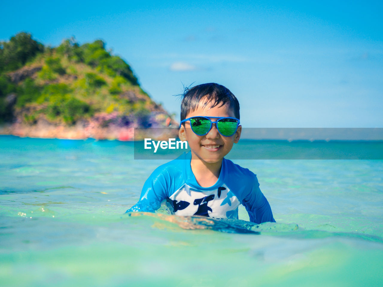 Portrait of boy wearing sunglasses swimming in sea against blue sky