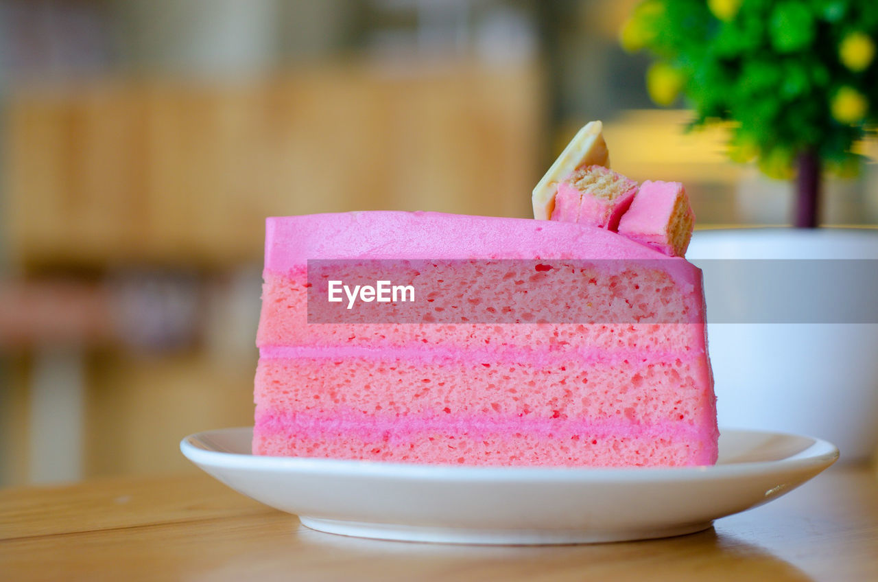 Pink cake on white disk with wood table, holiday time.