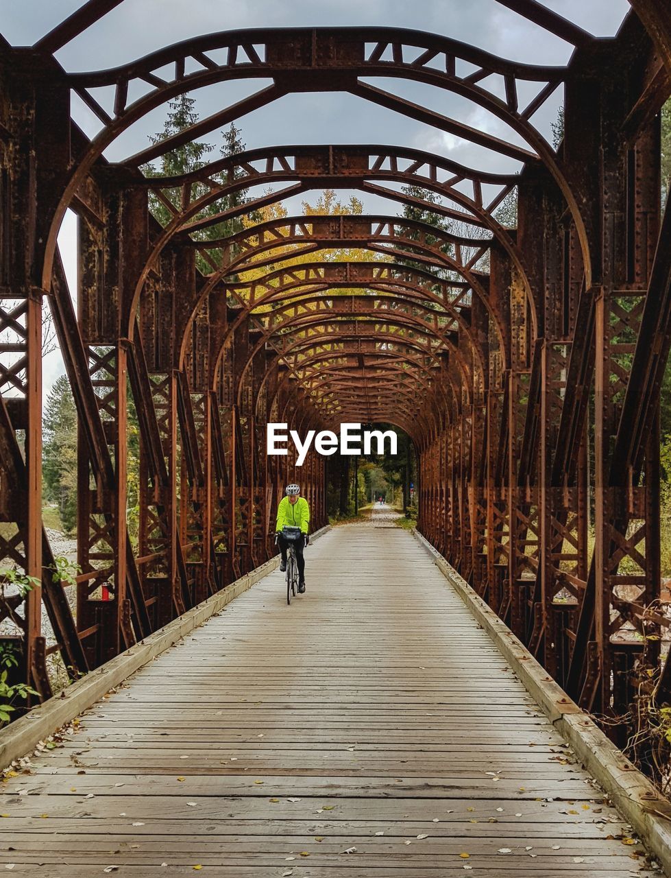 A man in a fluorescent yellow jacket riding a bike on an iron bridge.