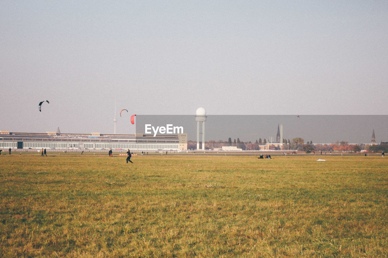 Tower and buildings in front of grassy field against clear sky