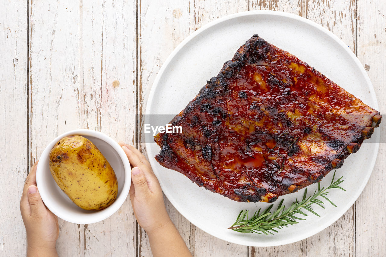 Roasted barbecue pork spare ribs with honey, oregano and rosemary in ceramic plate and baked potato