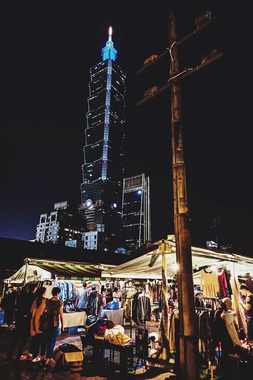 PEOPLE ON ILLUMINATED STREET AMIDST BUILDINGS AT NIGHT