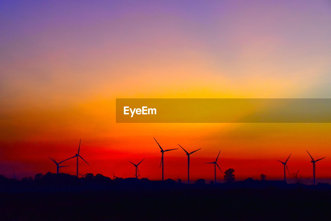 SILHOUETTE OF WIND TURBINES ON LAND AGAINST SKY DURING SUNSET