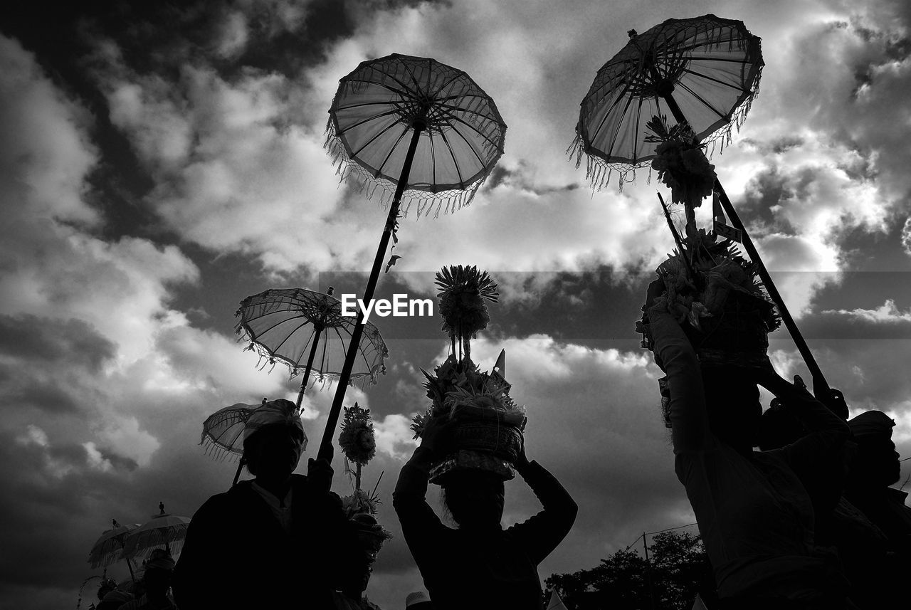 Low angle view of people with umbrella against cloudy sky during festival