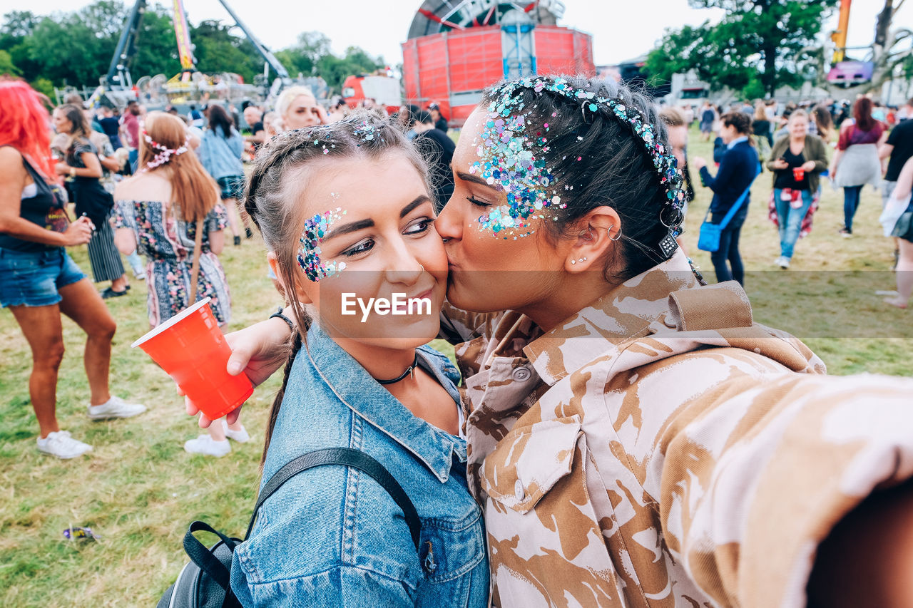 Woman with glitter kissing friend on field