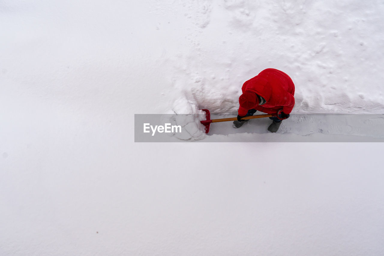 A woman in a red jacket cleans a path in the snow. view from above. 