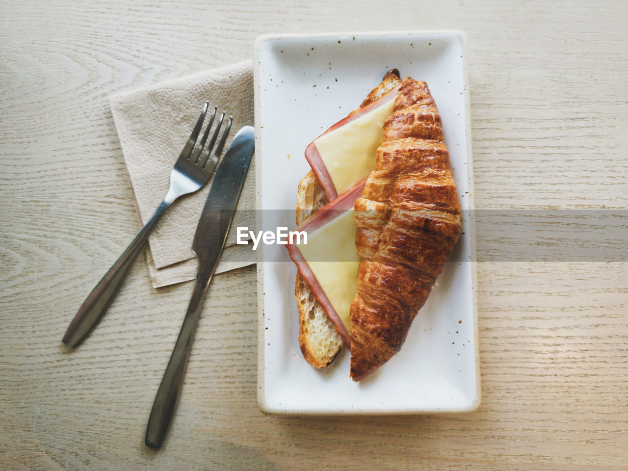 Croissant sandwich ham cheese on wooden table and fork knife