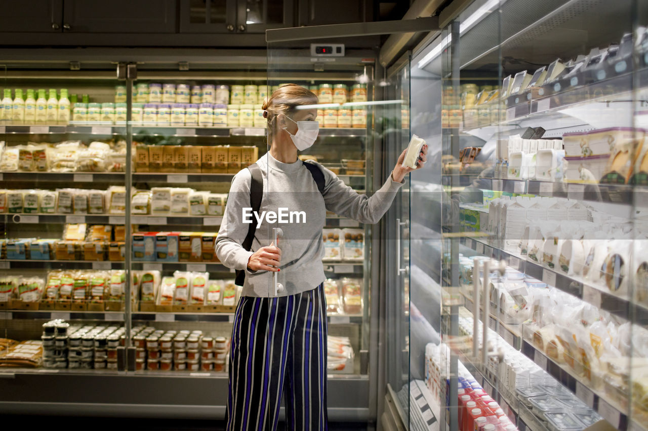 Female customer reading ingredient on product while shopping in supermarket during covid-19