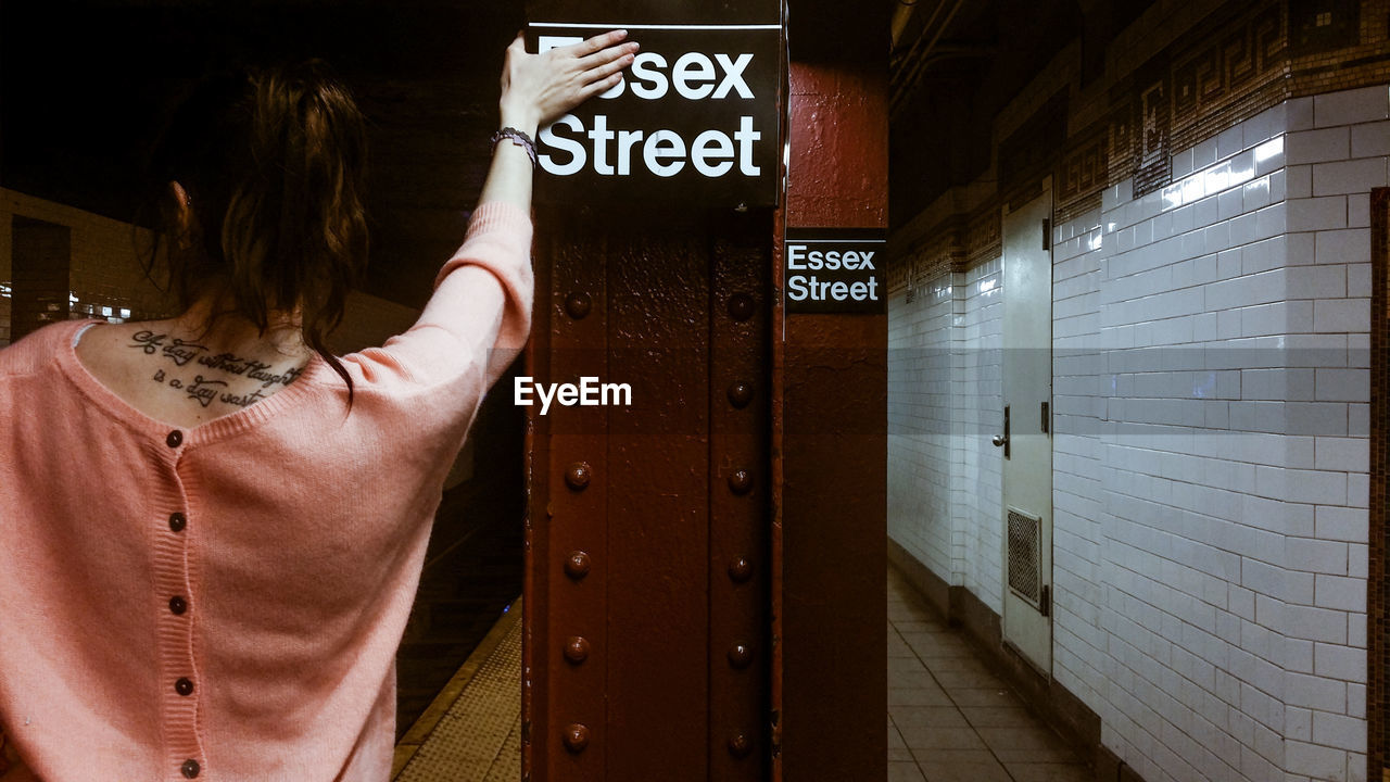 Rear view of woman standing while covering text at subway platform