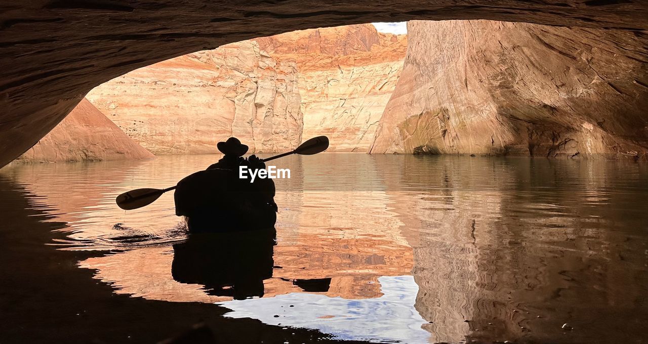 Rear view of silhouette man rafting in cave with paddle