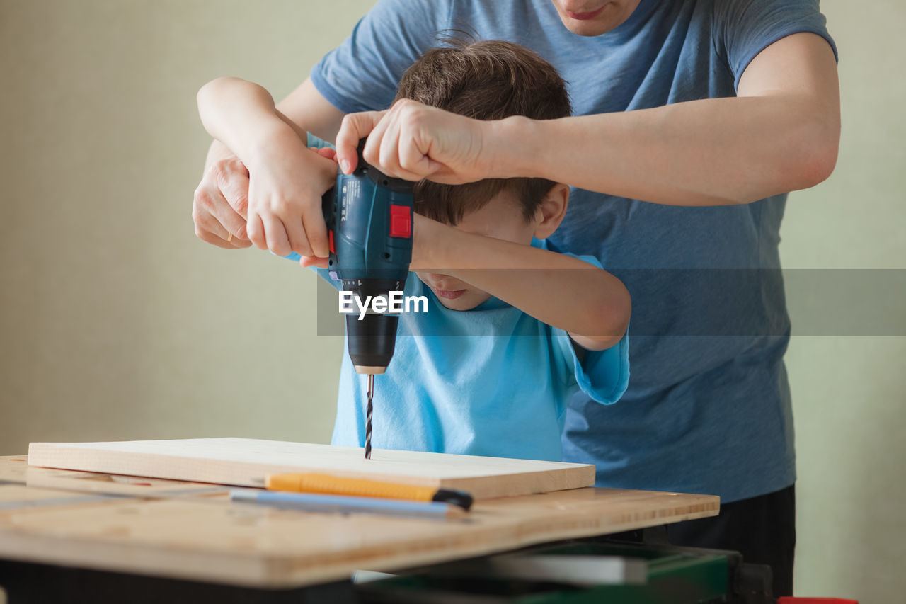 Dad and son work together while standing at workbench. little boy learning to drill.