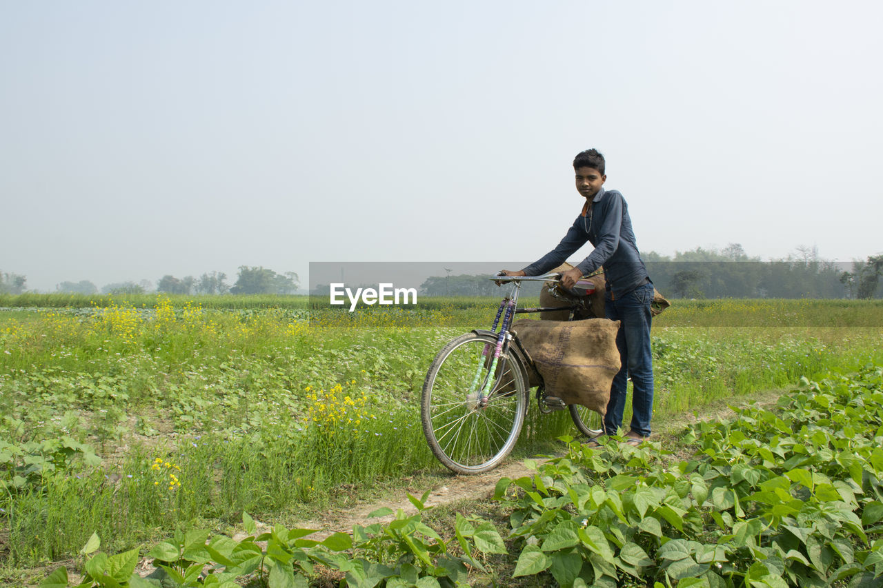 Young farmer riding bicycle carrying vegetable bag after harvest