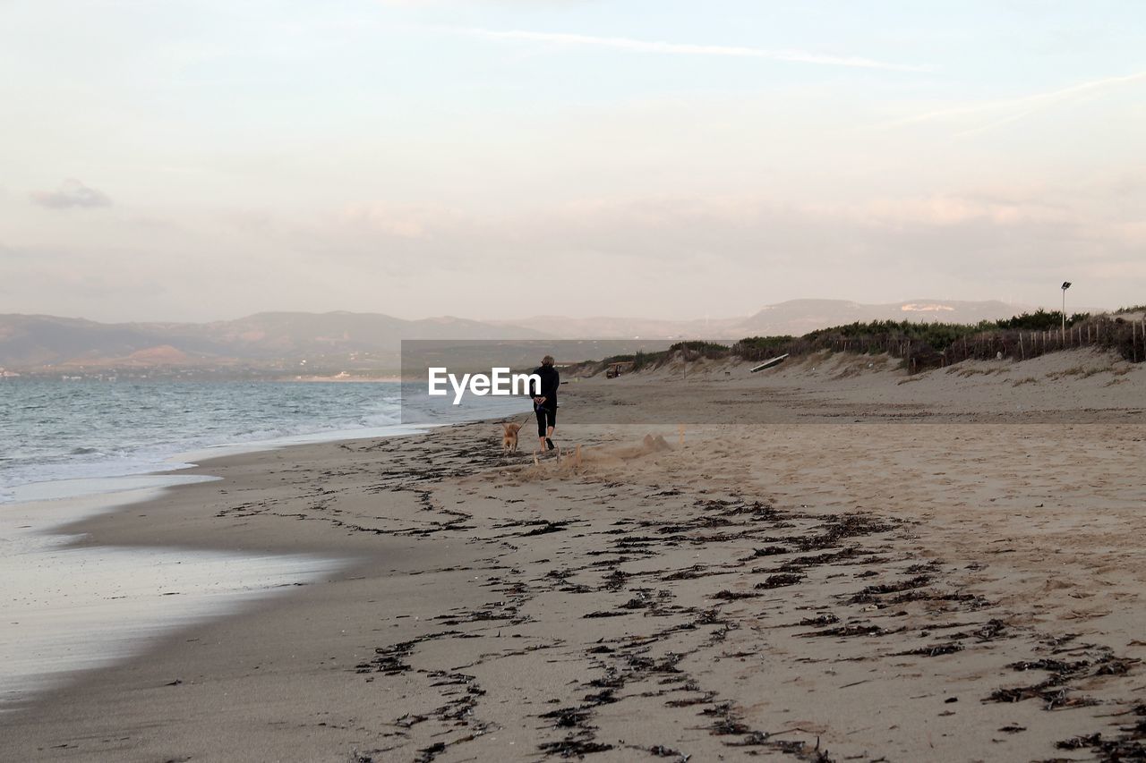 FULL LENGTH OF PERSON STANDING ON BEACH AGAINST SKY