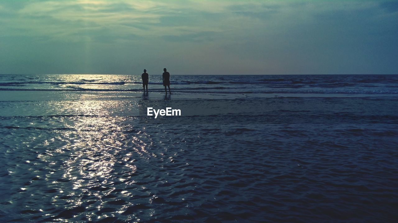 Silhouette men at beach against sky