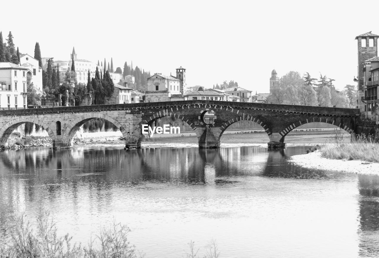 Arched bridge over river with built structures against clear sky