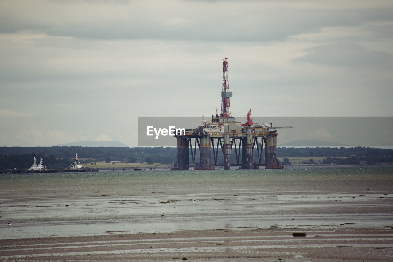 Oil drill amidst sea against sky