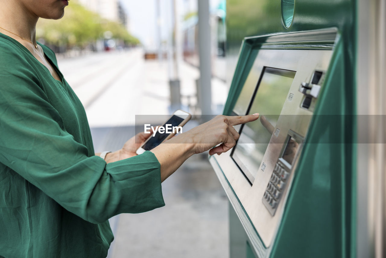 Woman with smart phone using ticket machine