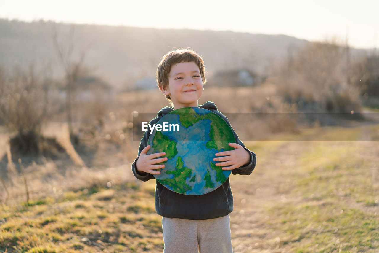 Portrait of cute boy holding globe against sky