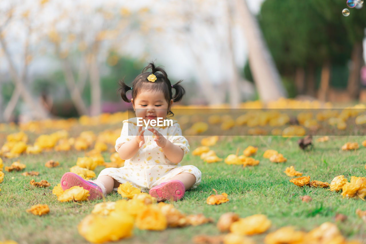 Cute girl sitting amidst flowers on field
