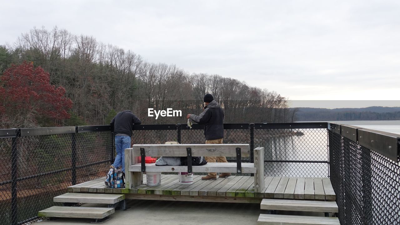 REAR VIEW OF COUPLE ON RAILING AGAINST SKY