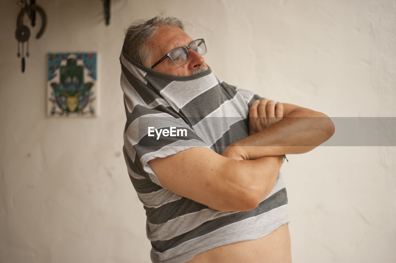 Senior man removing striped t-shirt at home