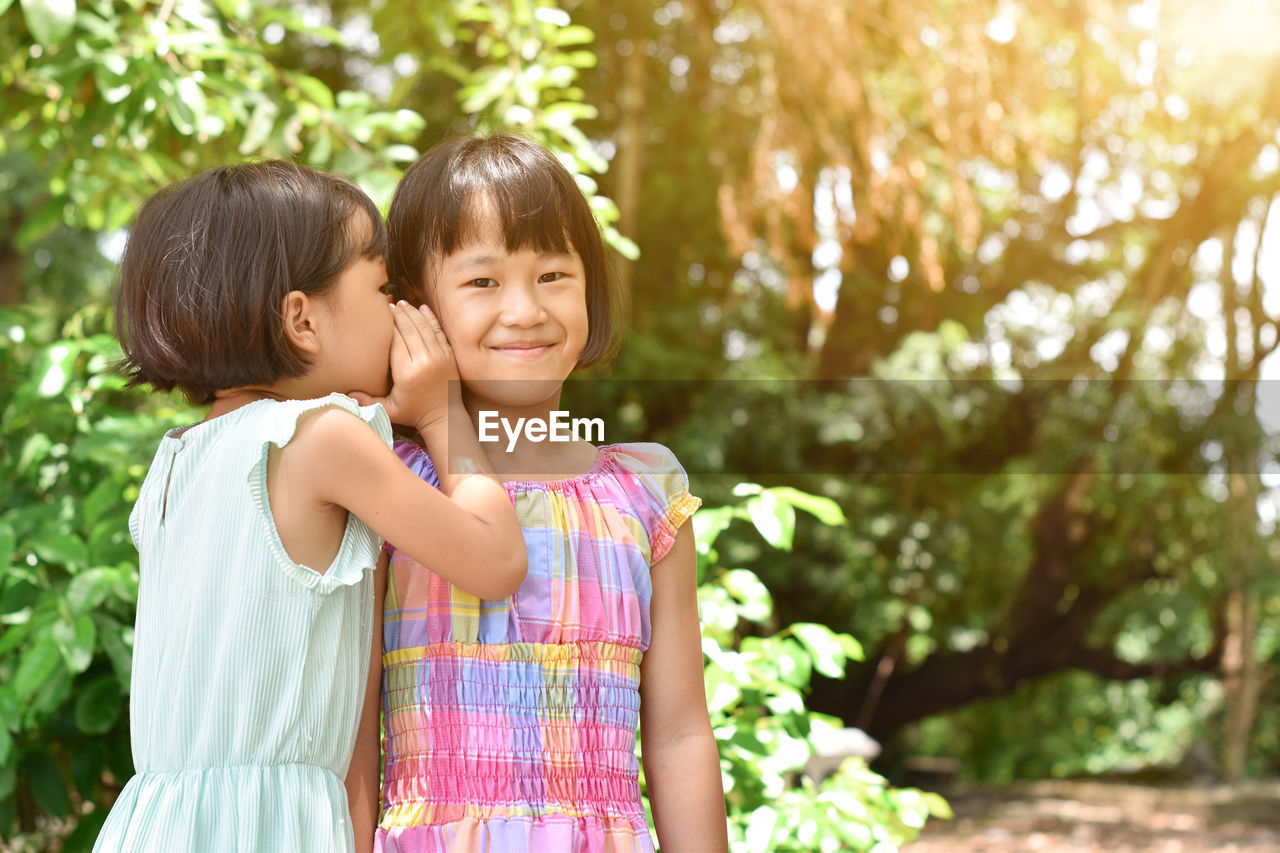 Cute girl whispering in sisters ear outdoors