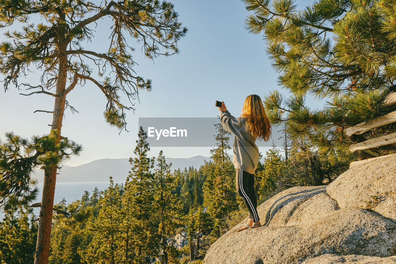 Young woman taking a picture of sunset over lake tahoe.