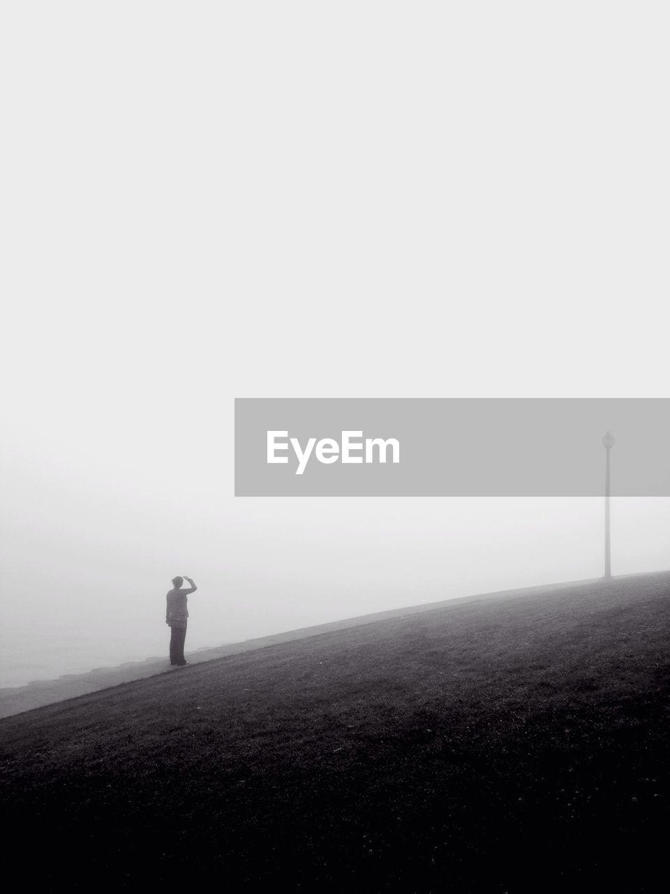 Woman standing on hill against sky during foggy weather