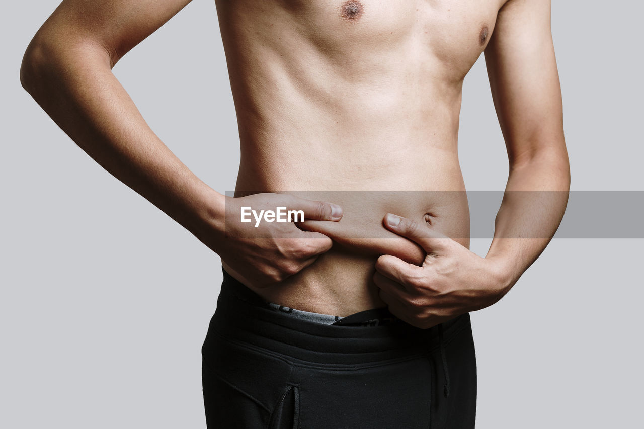 Midsection of shirtless man standing against gray background