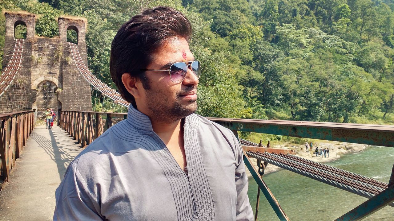 Man in sunglasses standing on bridge against trees