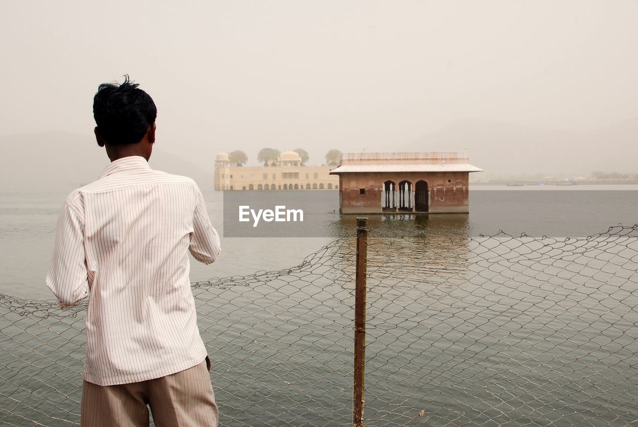 REAR VIEW OF MAN STANDING AGAINST SEA