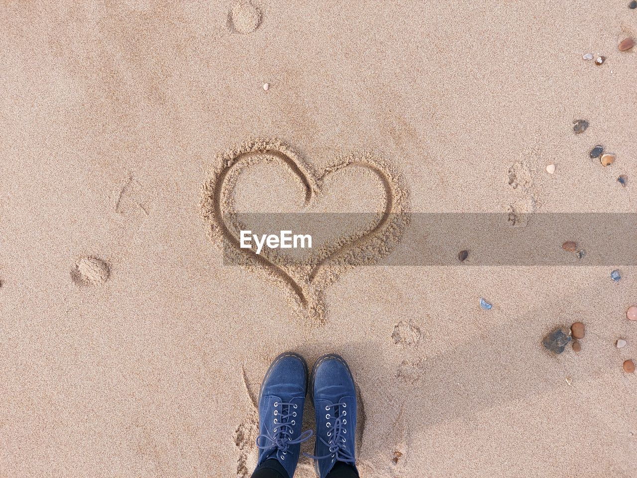 LOW SECTION OF PERSON STANDING BY HEART SHAPE ON SAND