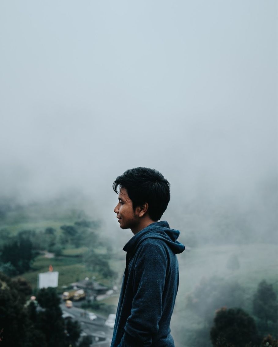 SIDE VIEW OF YOUNG MAN STANDING AGAINST MOUNTAIN