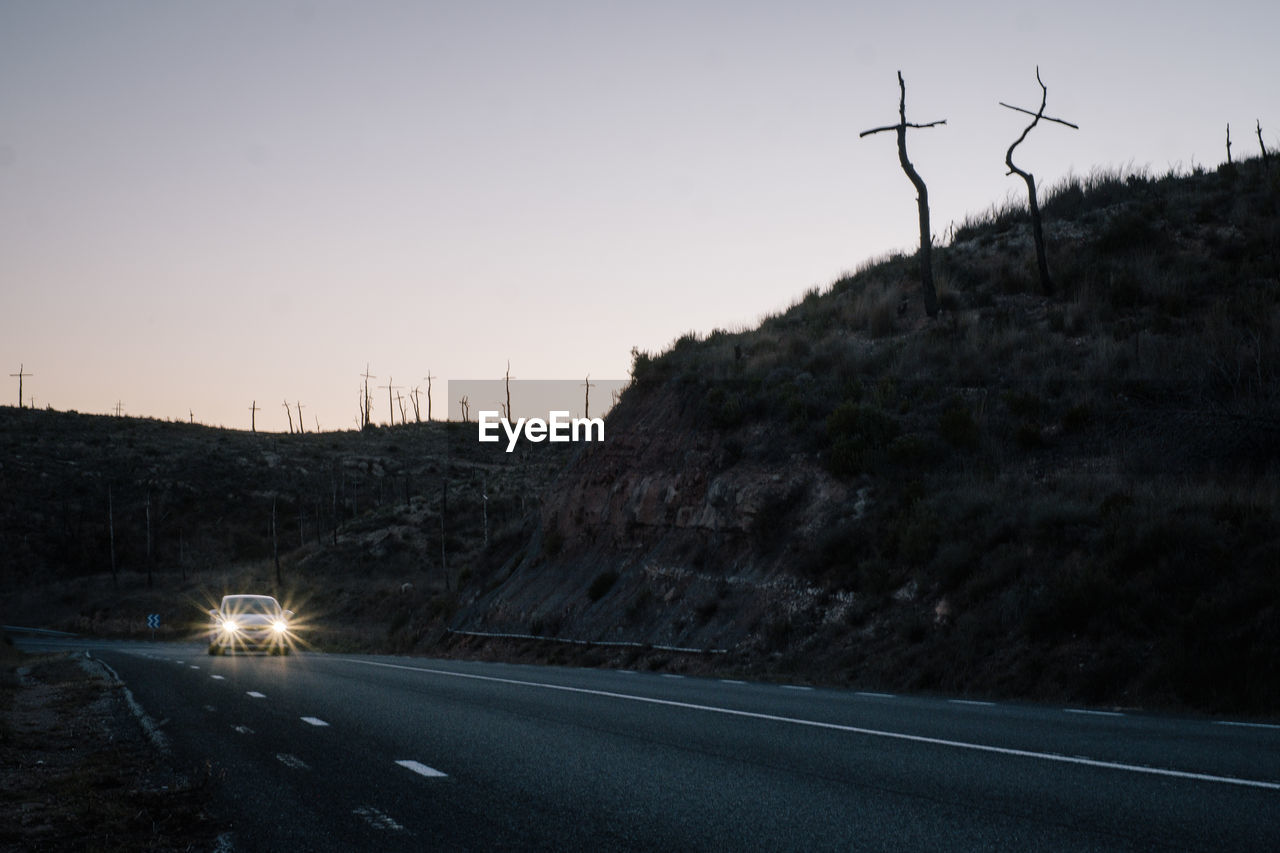 Car moving on country road by hill during sunset