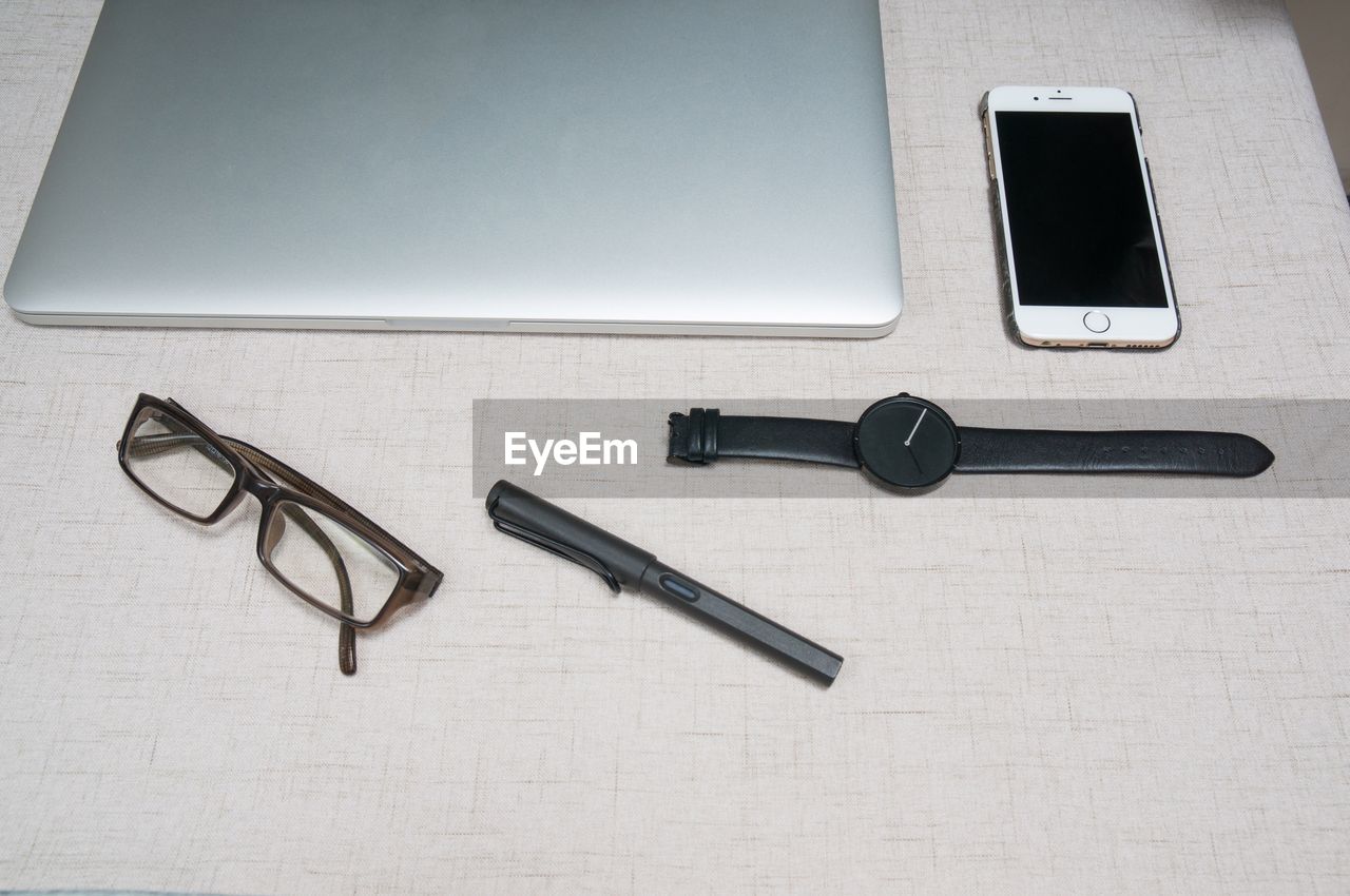 High angle view of mobile phone with laptop and eyeglasses on desk