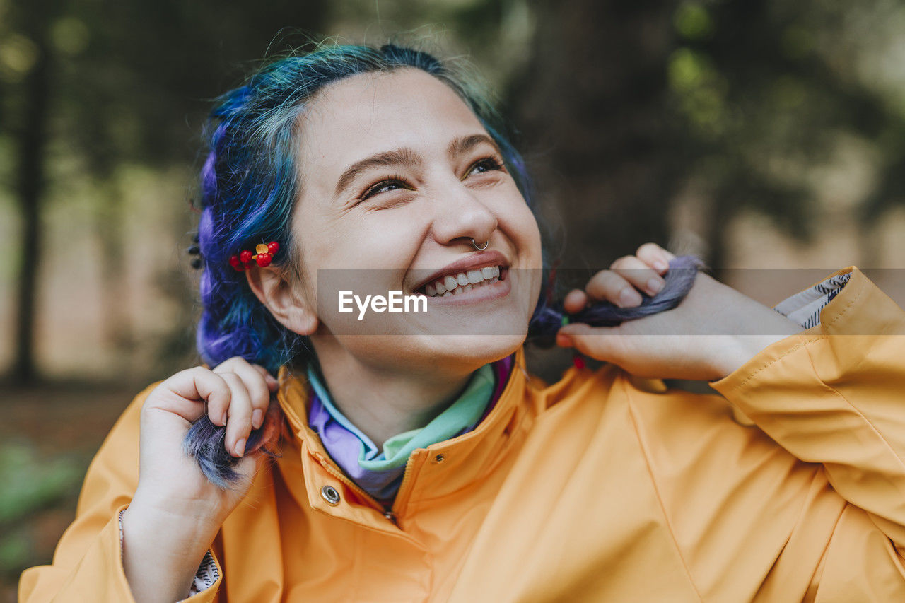 Cheerful woman playing with braided hair in forest