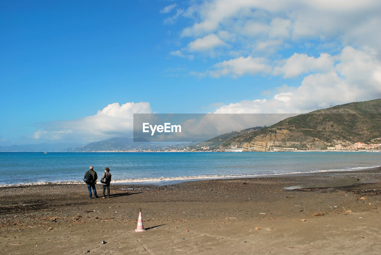 PEOPLE RELAXING ON BEACH AGAINST BLUE SKY